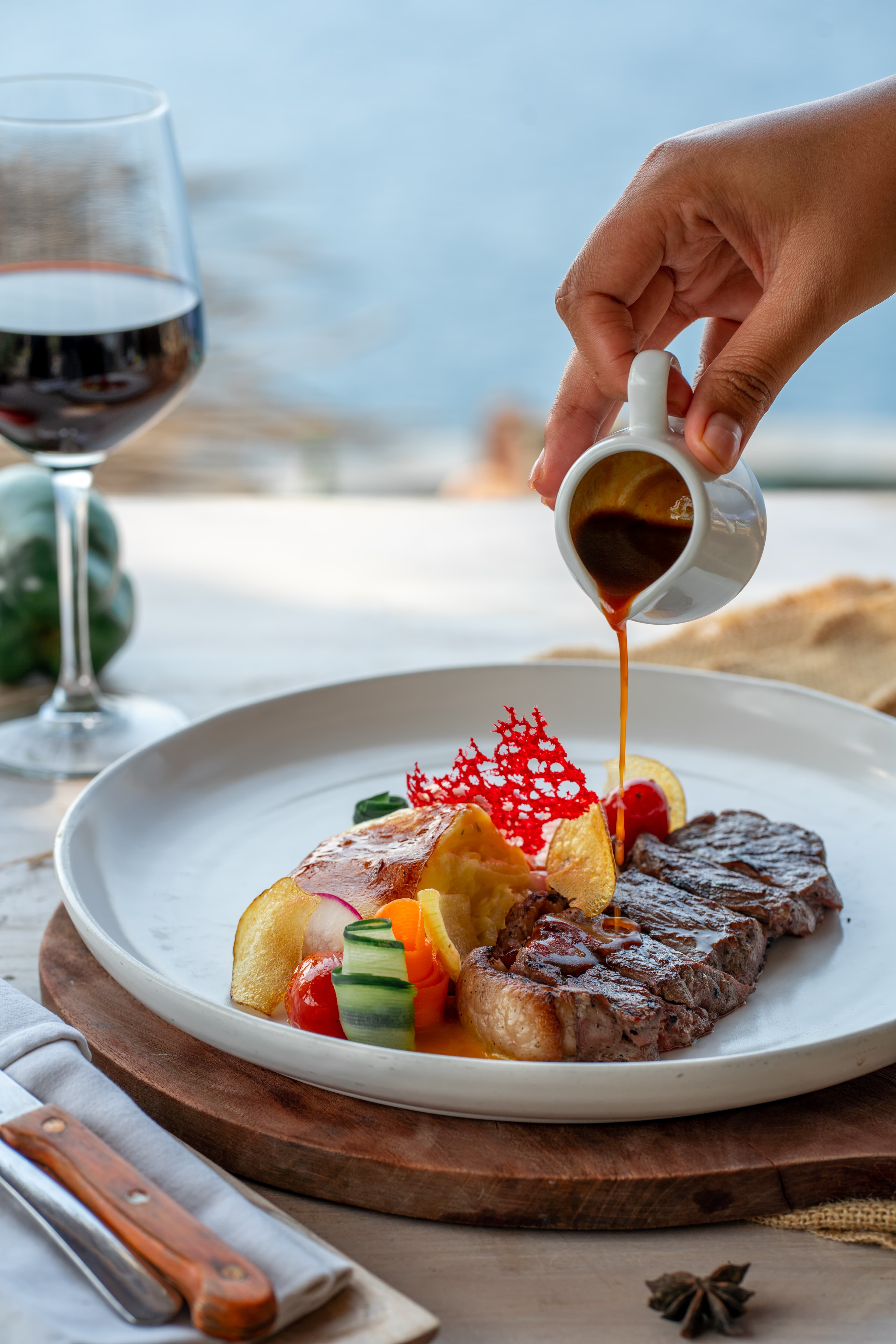 A hand pours rich gravy over sliced steak served with potato gratin and vegetables.