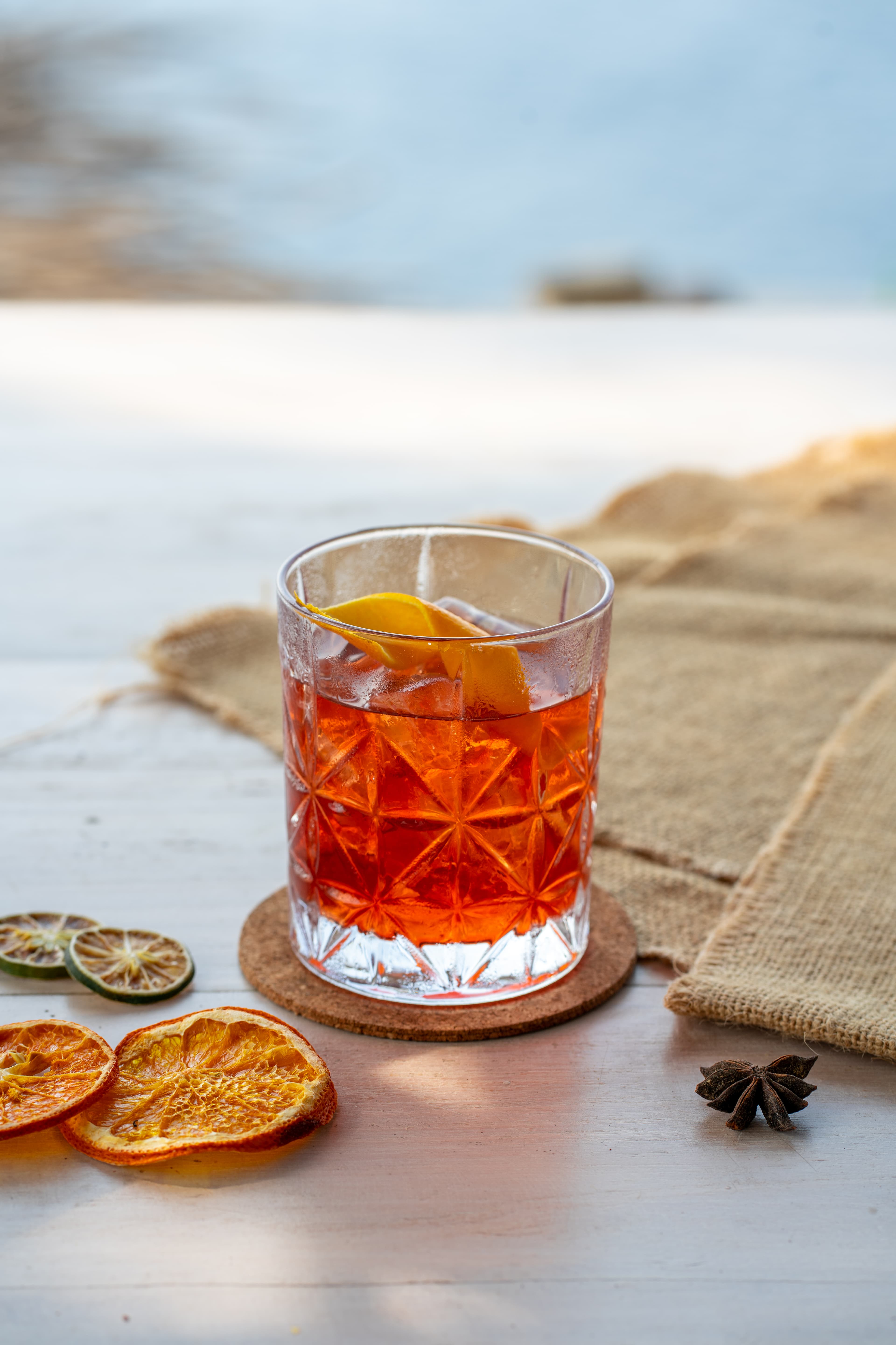 Refreshing orange cocktail with ice and citrus garnish on a sunny outdoor wooden table.