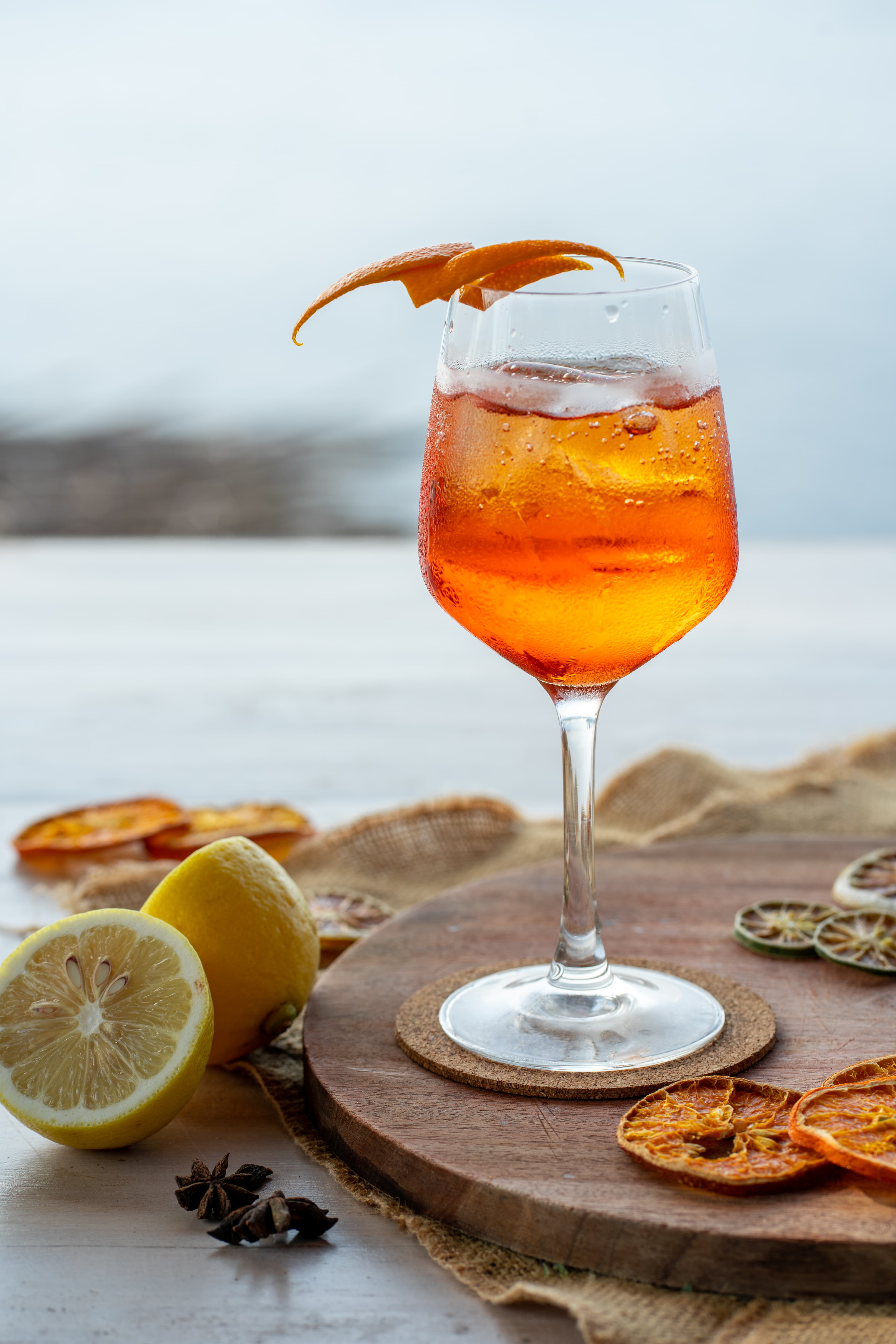 Chilled orange spritz cocktail with ice and citrus garnish on a rustic wooden board.