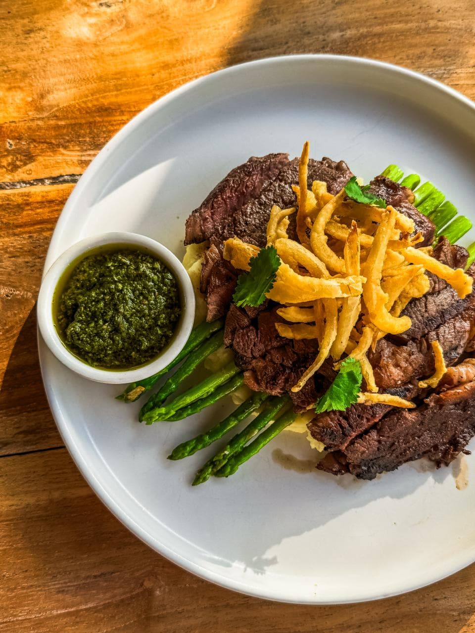 Grilled steak topped with crispy onions, served with asparagus and a side of chimichurri.